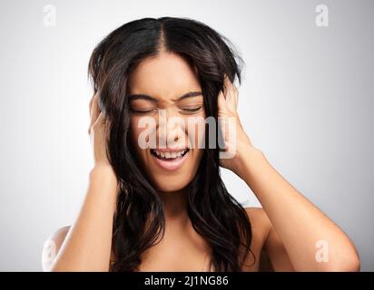 Ihr Haar ist verrückt. Ausgeschnittene Aufnahme einer attraktiven jungen Frau, die vor grauem Hintergrund im Studio posiert. Stockfoto