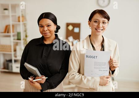 Porträt einer weiblichen Mannschaft, die lächelt und die Kamera anlächelt, während sie die Geschäfte in minimalem Büroinnenraum führt Stockfoto