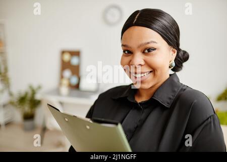 Nahaufnahme des Porträts einer erfolgreichen schwarzen Geschäftsfrau, die lächelt, während sie in einem minimalistischen Büro steht Stockfoto