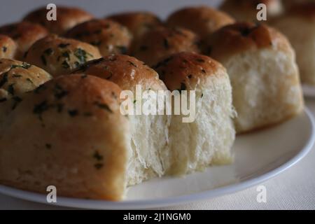 Brötchen zum Abendessen. Hausgemachte, goldbraune, frisch aus dem Ofen gebackene, mit Butter glasierte Esbrolls. Aufgenommen auf weißem Hintergrund zusammen mit Korianderblättern Stockfoto