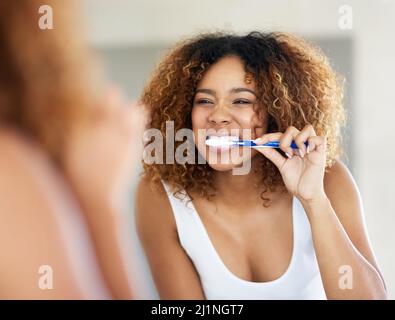 Bürsten ist das erste und letzte, was ich tue. Aufnahme einer jungen Frau, die sich im Badezimmer die Zähne putzt. Stockfoto