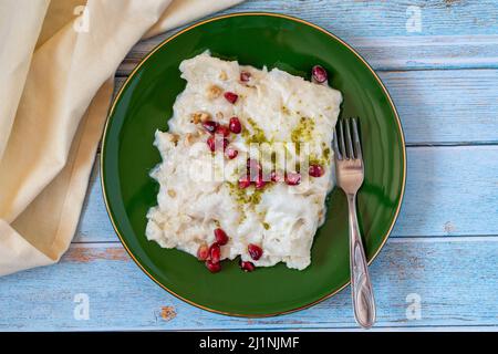 Gulac Dessert auf Holzhintergrund. Traditionelles Ramadan-Dessert. Güllaç Dessert mit Pistazie und Granatapfel verziert. Delikatessen der türkischen Küche. Stockfoto
