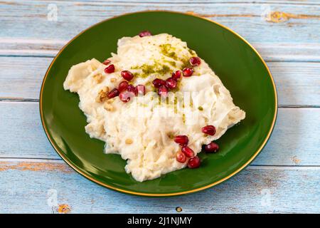 Gulac Dessert auf Holzhintergrund. Traditionelles Ramadan-Dessert. Güllaç Dessert mit Pistazie und Granatapfel verziert. Delikatessen der türkischen Küche. Stockfoto