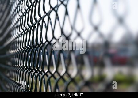 Nahaufnahme eines gewebten grünen kunststoffbeschichteten Eisendraht-Zauns in einem Feld mit dem Fokus links von der Mitte. Hintergrundbild Stockfoto