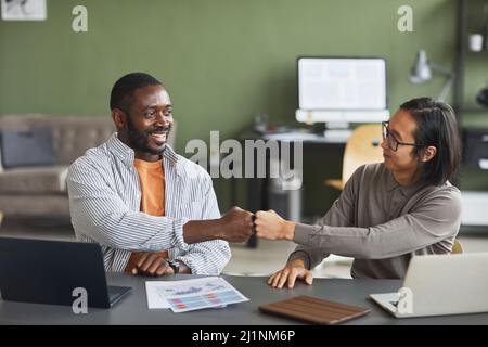 Vorderansicht Porträt von zwei ethnischen Geschäftsleuten afroamerikanischen und asiatischen Faust stoßen während der Zusammenarbeit im Büro Stockfoto