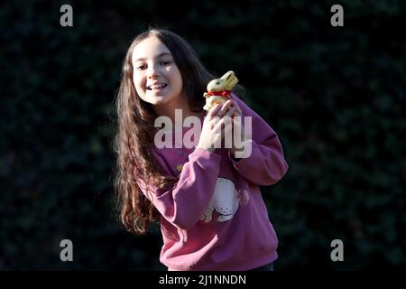 Genf, Schweiz - 03 07 2022 glückliches junges Mädchen mit goldenem osterhase auf Händen. Mädchen feiert Ostern Geschenk im Freien im Park oder Wald.Kleinkind Stockfoto