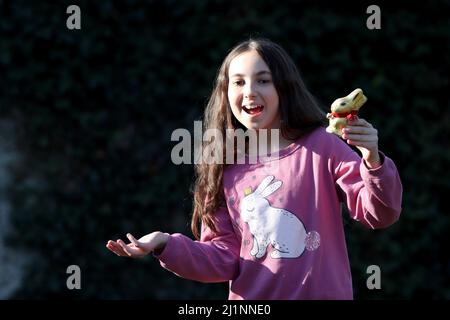 Genf, Schweiz - 03 07 2022 glückliches junges Mädchen mit goldenem osterhase auf Händen. Mädchen feiert Ostern Geschenk im Freien im Park oder Wald.Kleinkind Stockfoto