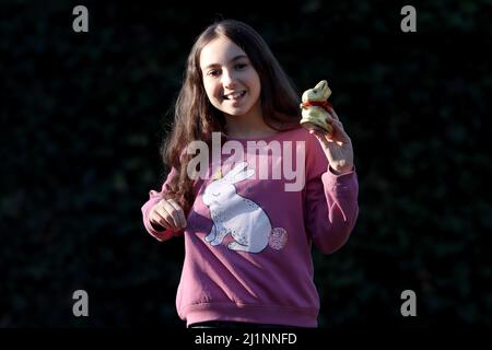 Genf, Schweiz - 03 07 2022 glückliches junges Mädchen mit goldenem osterhase auf Händen. Mädchen feiert Ostern Geschenk im Freien im Park oder Wald. Stockfoto