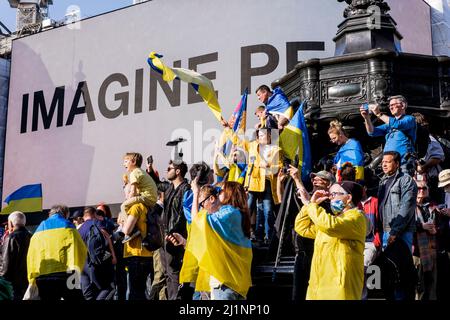 London, 26.. März 2022. Tausende von Menschen treten mit der Ukraine zusammen, marschieren und mahnten im Zentrum von London, um gegen die russische Invasion zu protestieren. Die Marschierenden versammeln sich am Piccadilly Circus, wo Yoko Onos ‘IMAGINE PEACE’ Kunstwerk auf den Bildschirmen zu sehen ist. Stockfoto