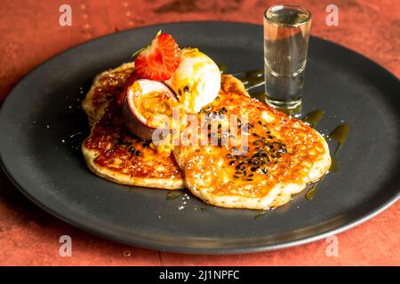 Eine Nahaufnahme von Pfannkuchen mit Erdbeeren, einer Passionsfrucht und Eis auf einem schwarzen Teller Stockfoto