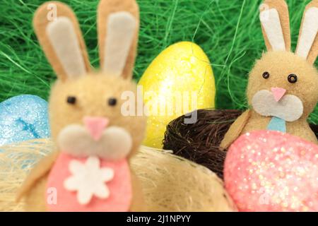 Zwei osterhasen in niedlichen Nestern, umgeben von bunten ostereiern. Stockfoto