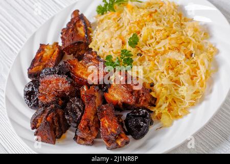 Geschmortes Sauerkraut mit Schweinefleisch und Pflaumen auf weißem Teller auf Holztisch, horizontale Ansicht von oben Stockfoto