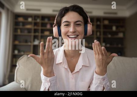 Positive Studentin in rosa Kopfhörern im Gespräch bei Videoanruf, Stockfoto