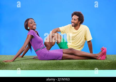 Sie färbt seine Welt. Ein junges afrikanisches Paar, das zusammen auf dem Gras sitzt. Stockfoto