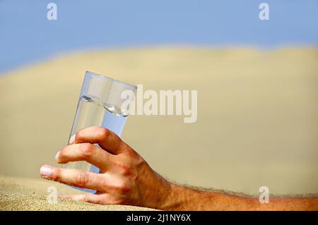 Hand hält ein frisches Glas kaltes Wasser in Wüste. Stockfoto