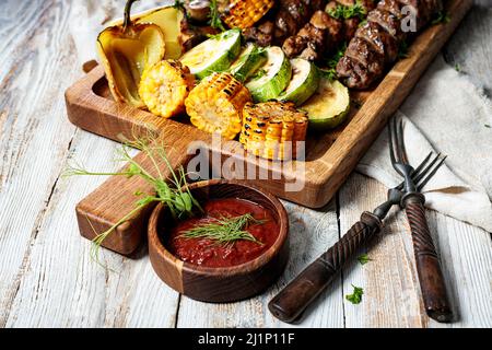 Verschiedene Kebabs mit gegrilltem Gemüse und Kräutern. Appetitlich gebratenes Fleisch, Mais, Zucchini und Pilze. Nahaufnahme Stockfoto
