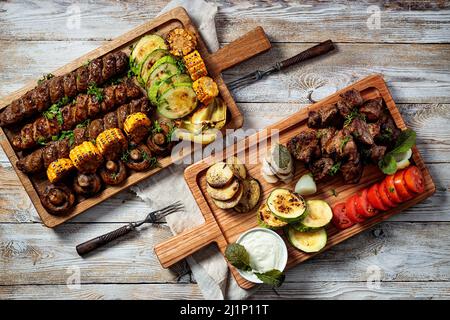 Verschiedene Kebabs, gegrilltes Fleisch mit Gemüse und Kräutern. Appetitlich gebratenes Fleisch, Tomaten, Zucchini, Kartoffeln und Zwiebeln auf Schneidebrettern. Draufsicht Stockfoto