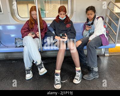 Drei Teenager-Gymnasiasten, die nach der Schule in Brooklyn, New York, einen F-Zug gefahren sind, waren mit ihren Handys unterwegs. Stockfoto