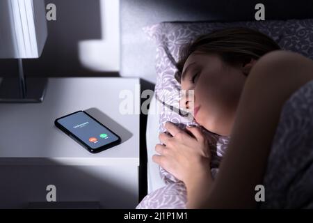 Telefonanruf eines unbekannten Anrufers in der Nacht, während die Frau im Bett schläft. Betrug, Betrug oder Handybetrug aufgrund verdächtiger gefälschter Nummern. Illegale mobile Kriminalität. Stockfoto