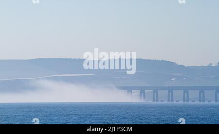 Dundee, Tayside, Schottland, Großbritannien. 27.. März 2022. Wetter in Großbritannien: Aufgrund der kalten Luft aus dem Westen bildet sich über den Fluss Tay dichter Nebel, der atemberaubende Ausblicke über Dundee bietet. Die Temperaturen fielen auf 14 Grad Später am Tag zerstreut die Sonne den Nebel, so dass der warme Sonnenschein scheint und die Temperaturen in Nordostschottland 18 Grad erreichen Spektakuläre Ausblicke von der Dundee-Uferpromenade auf die Tay Road Bridge, den Tay River, die Tay Railway Bridge und das V&A Design Museum im Frühjahr. Kredit: Dundee Photographics/Alamy Live Nachrichten Stockfoto