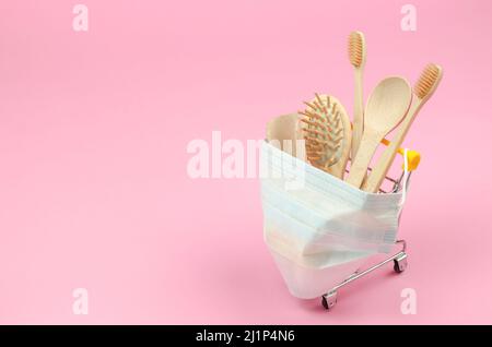 Das Konzept, ökologische Produkte im Internet zu kaufen. Körperpflegeartikel aus Holz in einem Einkaufswagen mit einer schützenden medizinischen Maske auf einem rosa b Stockfoto