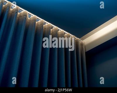 Nahaufnahme des blauen Wandvorhangs an der Gardinenstange, dekoriert mit verstecktem Licht unter der Decke in der Nähe der Wand in der blauen Zimmerecke. Stockfoto