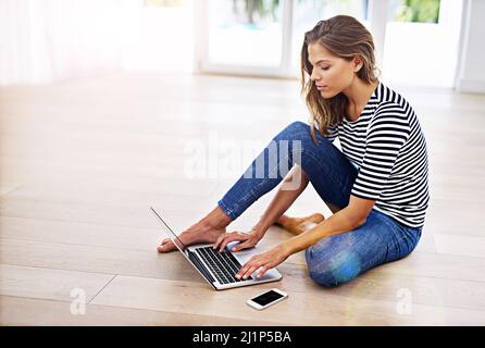 Shes ein technisch versierter Surfer. Aufnahme einer jungen Frau, die mit ihrem Handy und Laptop auf dem Boden sitzt. Stockfoto