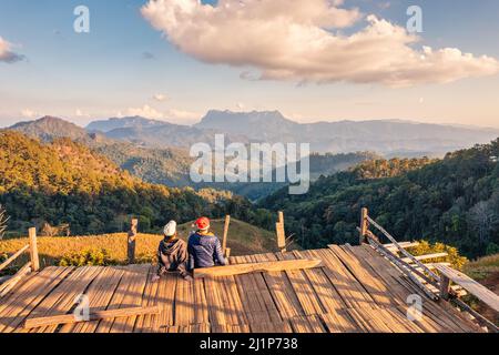 Rückansicht des asiatischen Paares, das abends auf dem Land den Blick auf die Berge auf dem Holzbalkon genießt. Hadubi ViewPoint, Wiang Haeng, Chiang Mai, Thailand Stockfoto