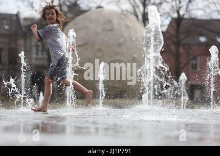 Aschersleben, Deutschland. 27. März 2022. Eine Wasserfontäne sorgt für Erfrischung in einem Stadtpark in Herrenbreite. Bei strahlendem Sonnenschein und warmen Temperaturen konnten viele Besucher den Frühling genießen. Quelle: Matthias Bein/dpa-Zentralbild/ZB/dpa/Alamy Live News Stockfoto