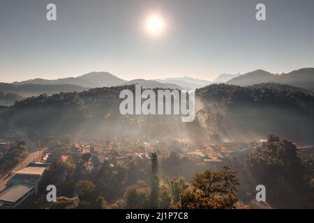 Luftaufnahme der Sonne über der Bergkette und neblig auf dem lokalen Dorf auf dem Hügel im tropischen Regenwald am Morgen Stockfoto