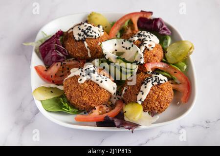 Frische Falafel mit Gemüse und Tsatziki-Sauce auf weißem Teller auf Marmortisch Stockfoto