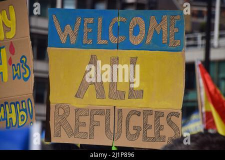 Das Plakat „Welcome All Refugees“ mit den Farben der Ukraine-Flagge ist während des marsches „London steht mit der Ukraine“ zu sehen. Tausende von Menschen marschierten aus Solidarität mit der Ukraine von der Park Lane zum Trafalgar Square, während Russland seinen Angriff fortsetzt. Stockfoto