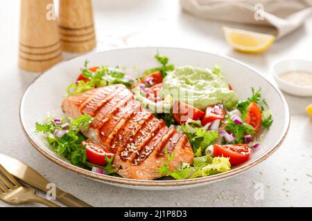 Gegrilltes Lachsfischfilet und frischer grüner Salat mit Gemüsestomaten und Avocado-Guacamole Stockfoto