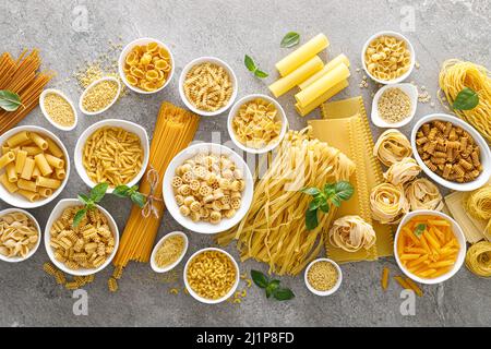 Pasta. Verschiedene Arten von ungekochten Nudeln und Nudeln auf steinernem Hintergrund, Draufsicht mit Platz für Text. Italienisches Essen kulinarisches Konzept. Sammlung Stockfoto