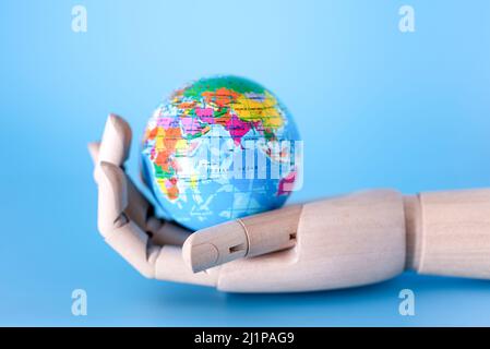 Nahaufnahme einer Holzhand, die einen Mini-Friedenskugel vor blauem Hintergrund hält. Das Konzept der Rettung der Erde. Stockfoto