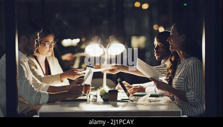 Arbeiten bis spät in die Nacht. Eine kurze Aufnahme einer Gruppe von Geschäftsleuten, die im Büro an einem Tisch arbeiten. Stockfoto