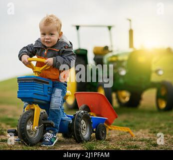 Nichts ist besser als eine Farm für einen Spielplatz. Porträt eines entzückenden kleinen Jungen, der auf einem Spielzeugauto auf einer Farm reitet. Stockfoto