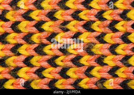 Synthetischer Strickstoff mit Musterelementen aus gelben, schwarzen und roten Garnen aus nächster Nähe. Mehrfarbig gemusterte Strickstruktur. Hintergrund Stockfoto