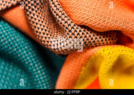 Ein Stapel mehrfarbiger synthetischer Strickstoffe mit verschiedenen Strukturen und Texturen. Ein Stapel von bunten Stoffen glatte Formen Hintergrund. Multicol Stockfoto