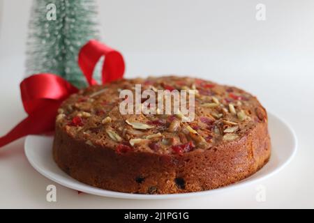 Obstkuchen mit Rum getränkten Früchten und Nüssen für weihnachten zubereitet. Aufgenommen mit Weihnachtsbaum, Kiefernkiefern und dekorativen Bändern im Hintergrund Stockfoto