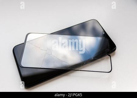 Der zerbrochene Schutzschild auf einem schwarzen Smartphone zeigt Display-Schutz und bruchsichere transparente Geräteprotektoren für die Crashsicherheit von Mobiltelefonen Stockfoto