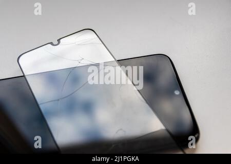 Der zerbrochene Schutzschild auf einem schwarzen Smartphone zeigt Display-Schutz und bruchsichere transparente Geräteprotektoren für die Crashsicherheit von Mobiltelefonen Stockfoto