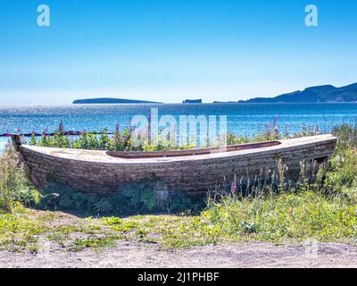 Altes Fischerboot mit Blick auf Rocher Perce weit im Hintergrund. Blick von der Straße 132 in der Nähe von Barachois, Perce, Quebec, Kanada. Gaspesie Region, Kanada. Stockfoto