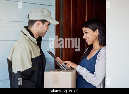 Protokollieren ihrer Lieferung als erhalten. Ausgeschnittene Aufnahme einer jungen Frau, die mit einem digitalen Tablet ihre Lieferung vom Kurier unterschreibt. Stockfoto