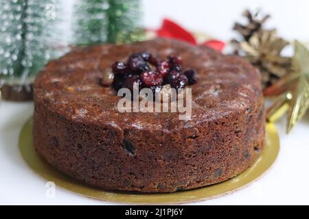 Reicher Plumenkuchen mit in Rum getränkten Früchten. Garniert mit Rum getränkten getrockneten Rosinen und Preiselbeeren. Aufgenommen mit festlichen Verzierungen auf weißem b Stockfoto