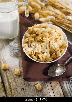 Schnelles Vollkornfrühstück. Auf einem Holztisch befinden sich Müslischoten in einer Schüssel, ein Krug mit Milch. Ein Haufen Getreide. Solarbeleuchtung. Es gibt niemanden im Phot Stockfoto