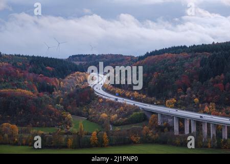 Deutsche Autobahnbrücke über das taubertal mit der Straße zwischen dem Wald in Herbstfarben. Im Hintergrund einige Windmühlen. Stockfoto