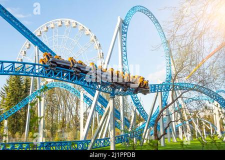 Der Vergnügungspark macht die Kreisbahn zum Drehfahren in einer spiralförmigen Achterbahn. Riesenrad im Hintergrund Stockfoto