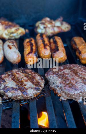 Burger und Würstchen, die auf dem Grill brutzeln Stockfoto