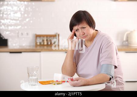 Kranke ältere Frauen kümmern sich um die Gesundheit, verwenden Sphygmomanometer zur Messung von Blutdruck, Puls und Herzfrequenz selbst und nehmen Medikamente zu Hause ein. Stockfoto